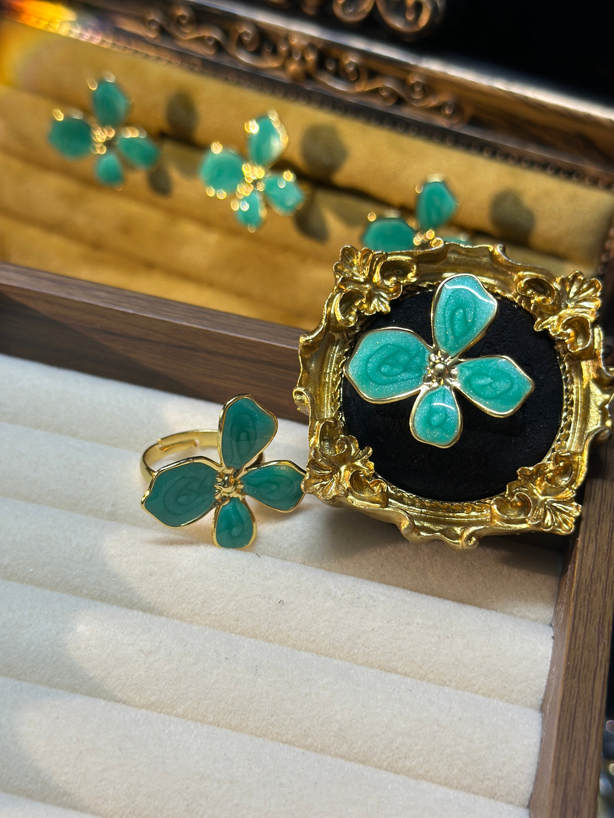 Teal green four-petal flower adjustable ring with raised swirling petal details and gold-tone centre