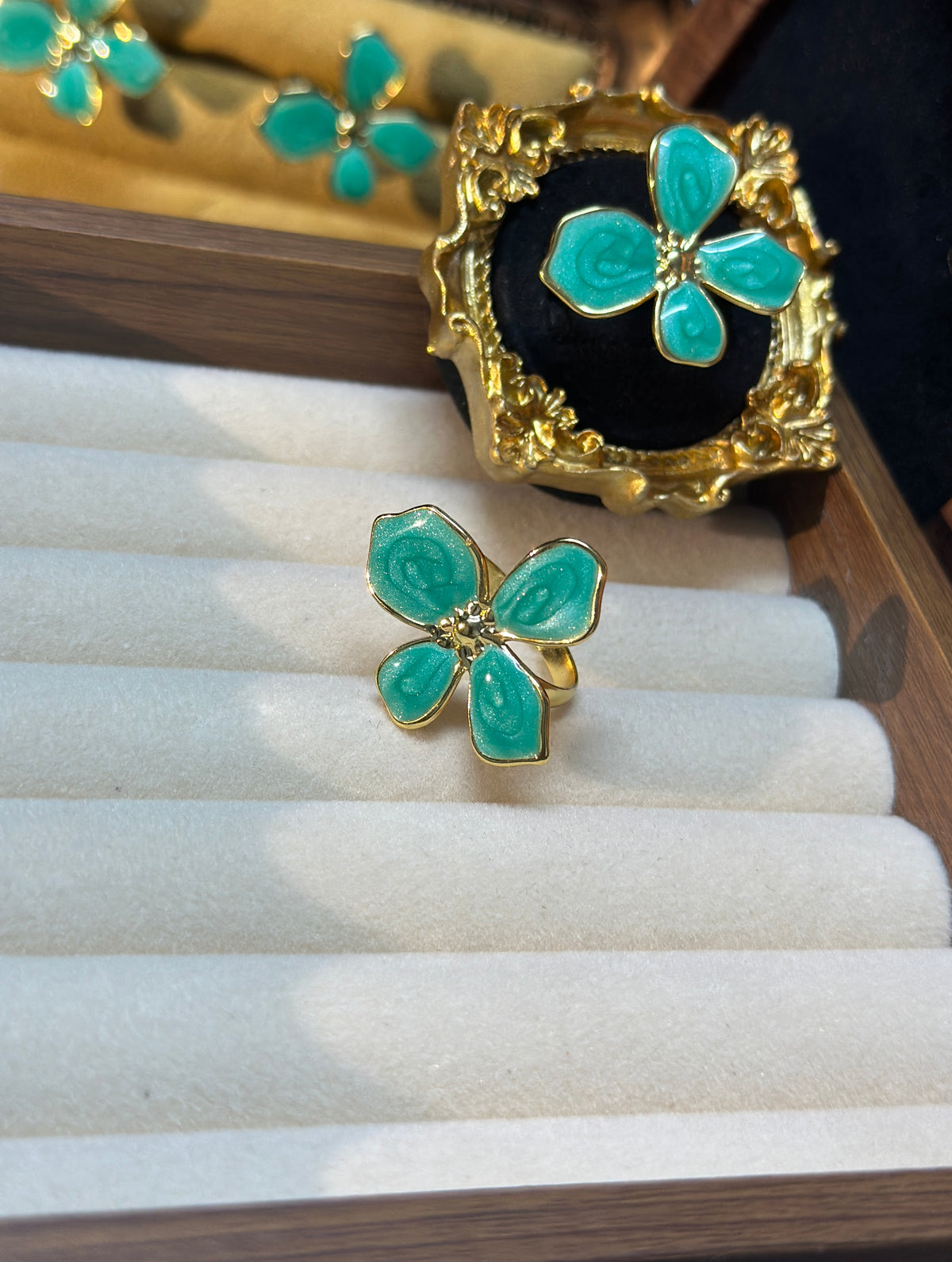 Teal green four-petal flower adjustable ring with raised swirling petal details and gold-tone centre