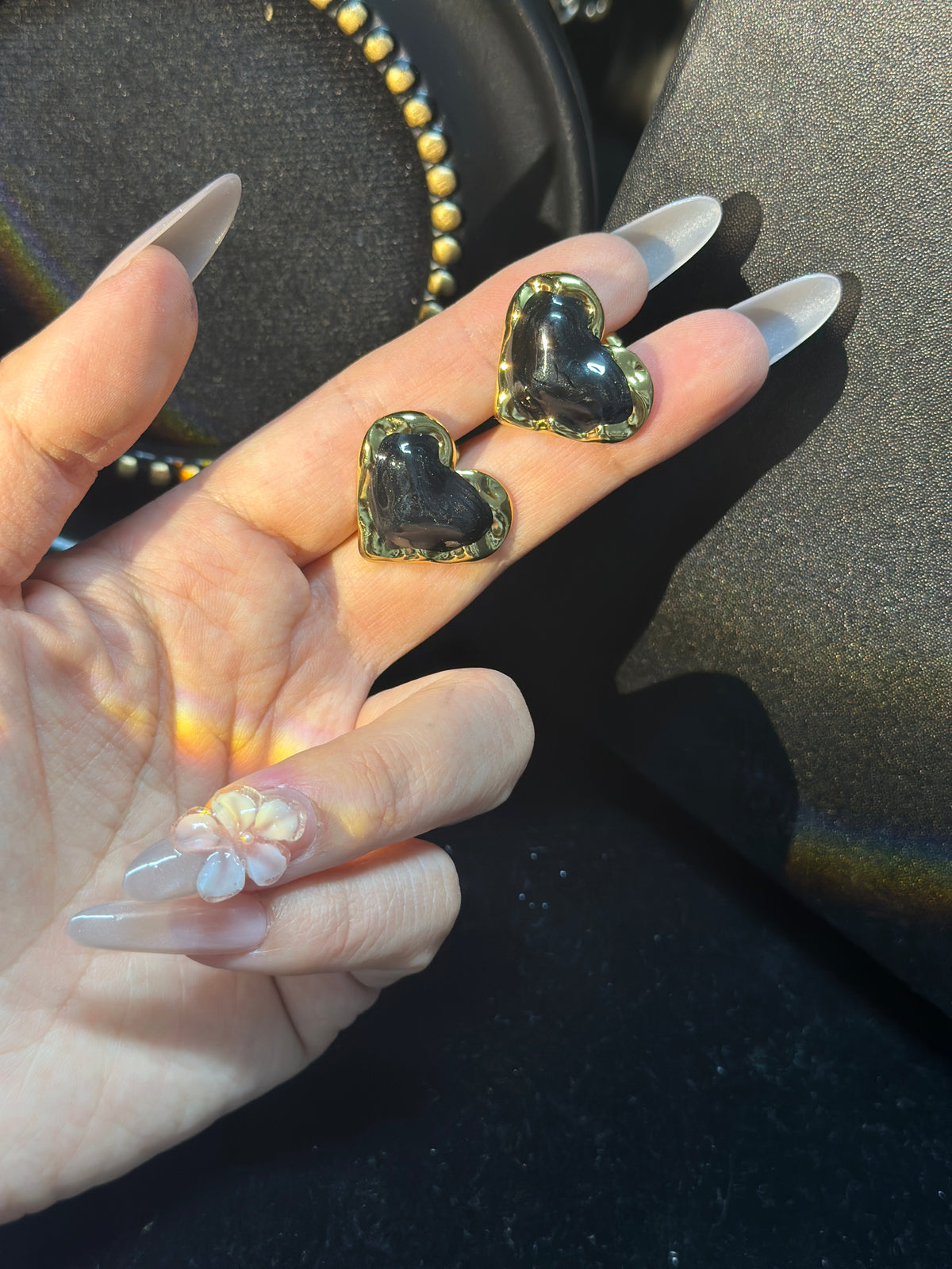 Black sculptural heart stud earrings with glossy black centres and polished gold-tone borders