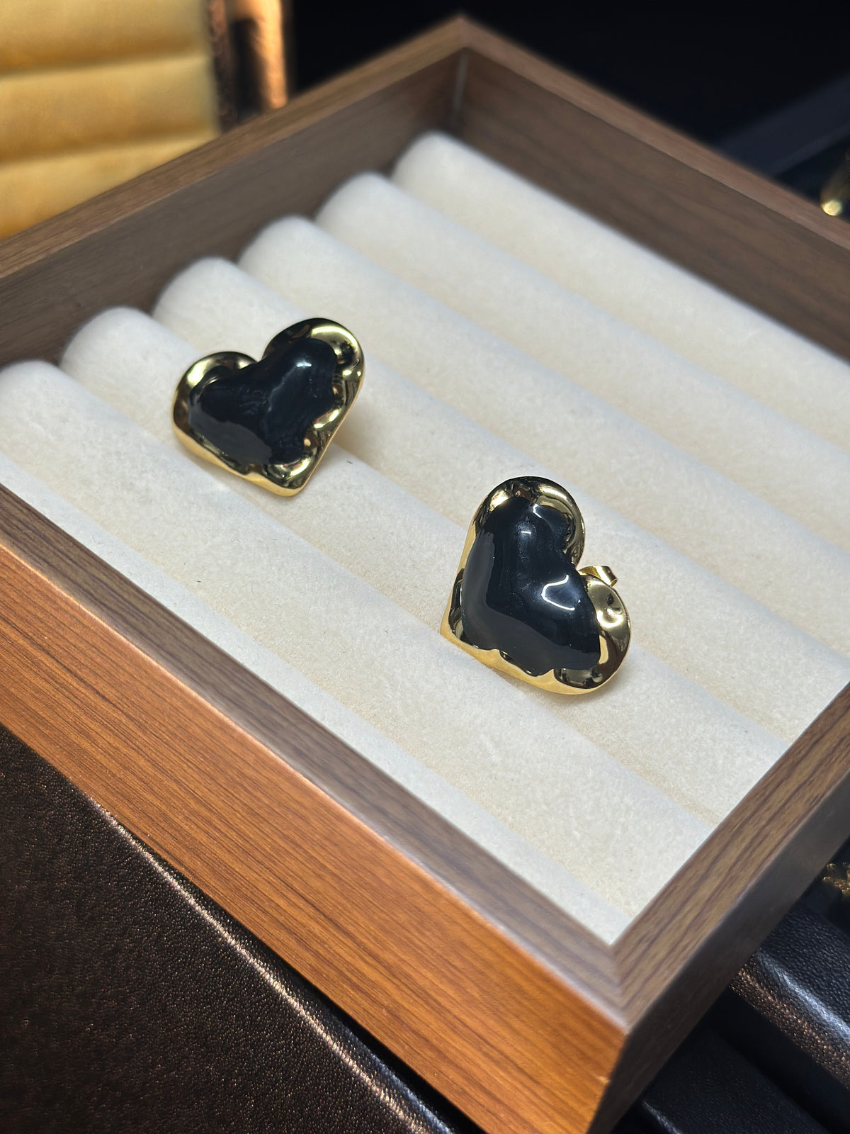Black sculptural heart stud earrings with glossy black centres and polished gold-tone borders