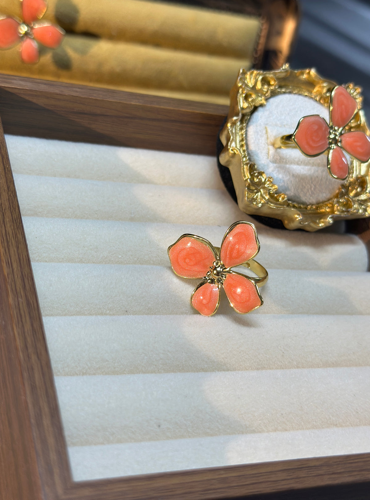 Coral pink four-petal flower adjustable ring with raised swirl detailing, gold-tone outlines and ornate decorative setting