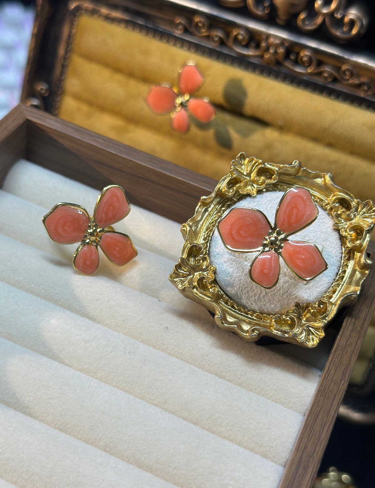 Coral pink four-petal flower adjustable ring with raised swirl detailing, gold-tone outlines and ornate decorative setting
