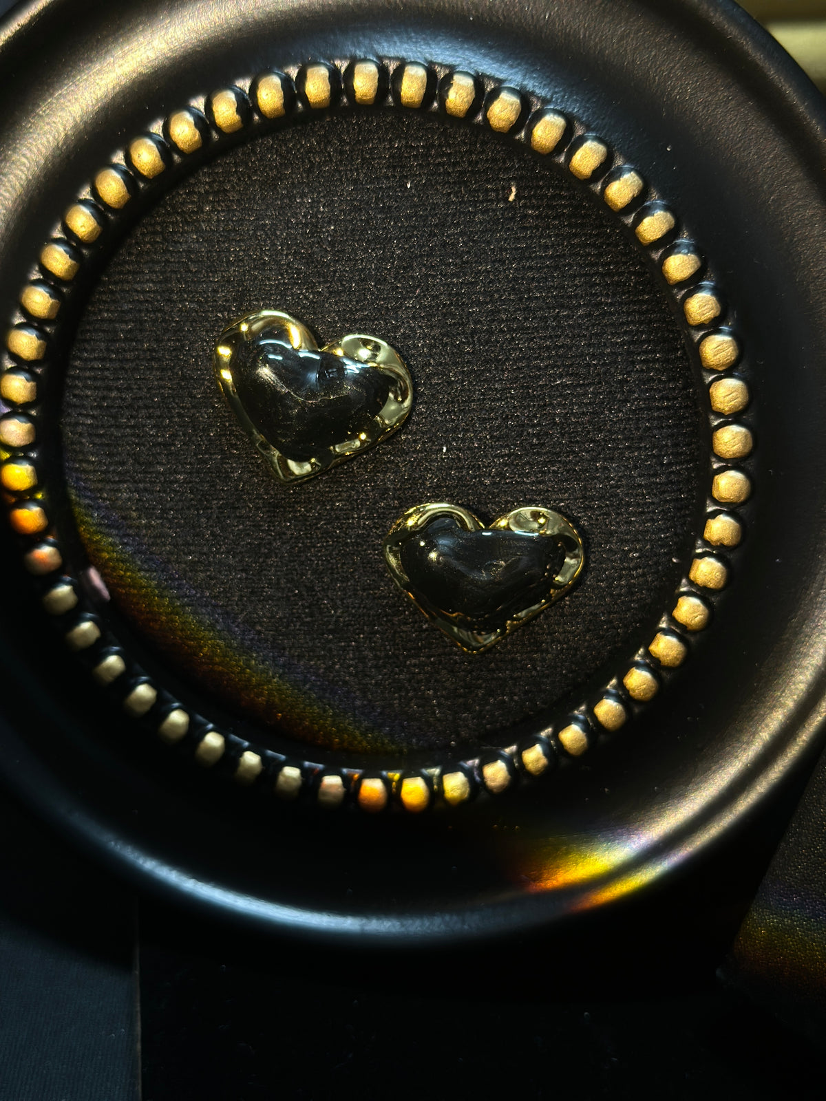 Black sculptural heart stud earrings with glossy black centres and polished gold-tone borders