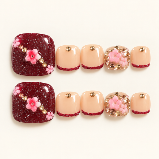 Burgundy glitter and nude-pink press-on toenails with pink floral decorations, burgundy glitter tips and gold-toned accents