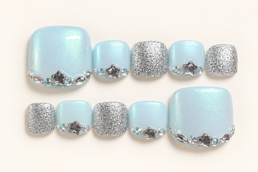Ice-blue pearlescent press-on toenails with silver glitter, star-shaped decorations and iridescent accents